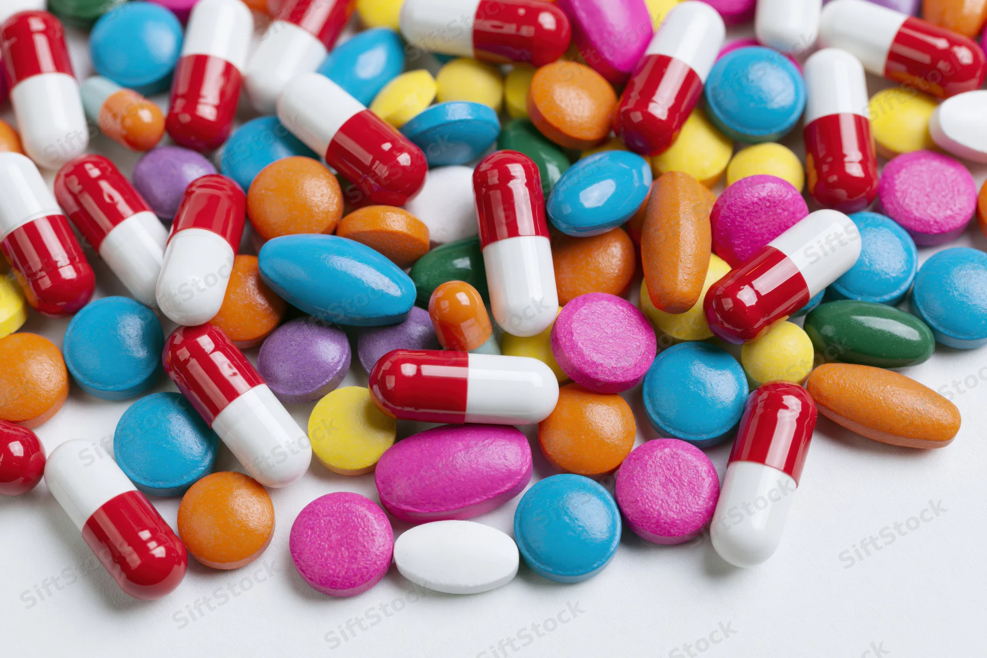 Assorted colorful pills and capsules scattered on white surface