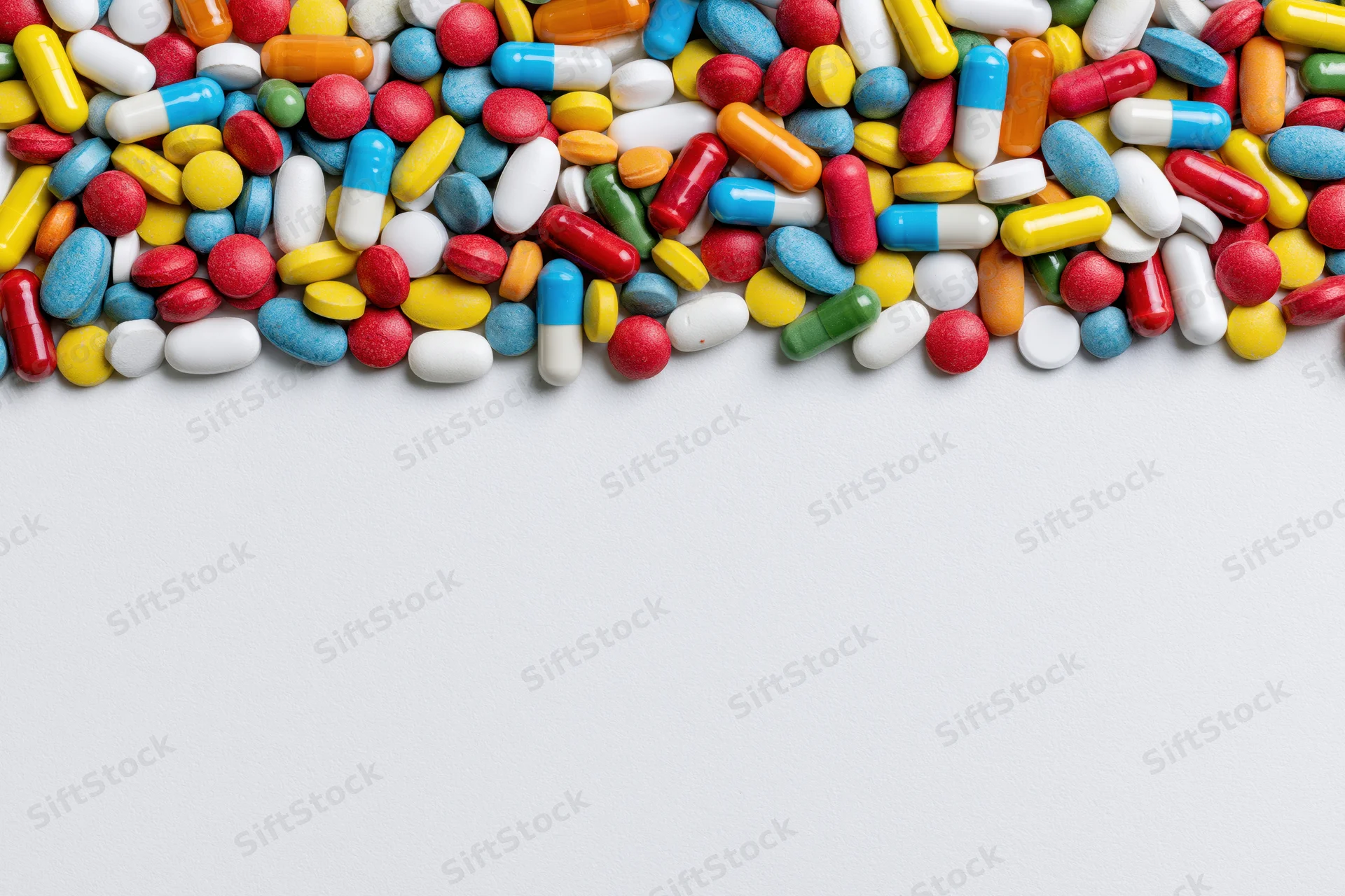 Assorted pharmaceutical pills and capsules scattered across white surface with copyspace below