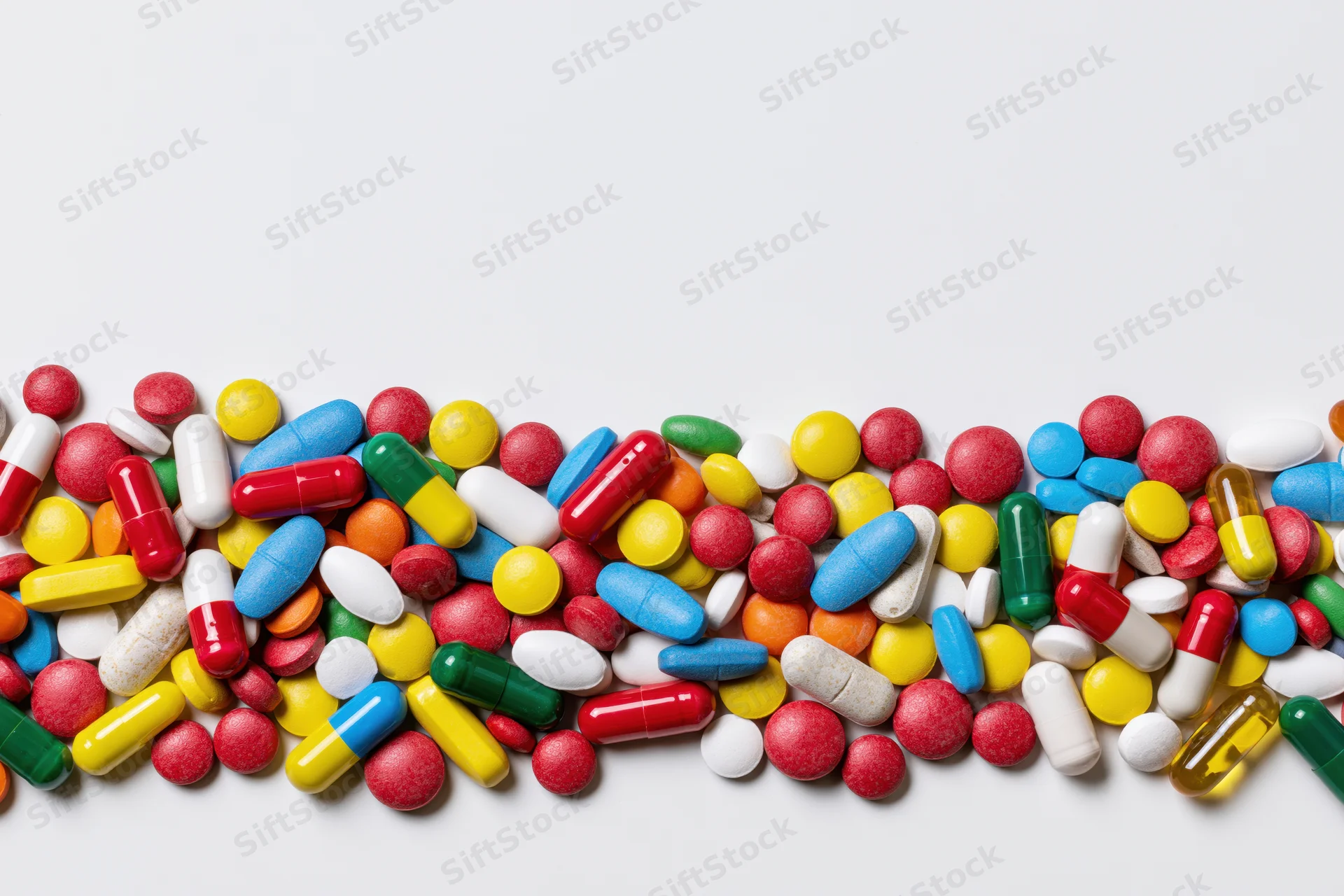Assorted pharmaceutical pills and capsules scattered in a row across a white surface