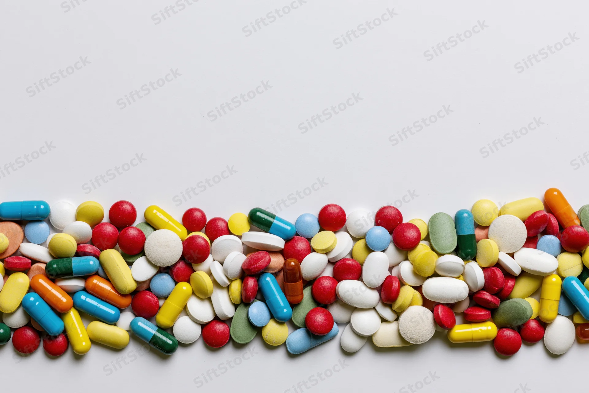 Assorted pharmaceutical pills and capsules scattered in a row on a white surface