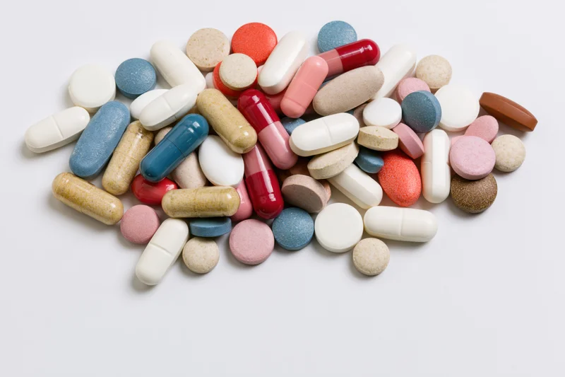 Assorted prescription pills and capsules scattered on a white surface