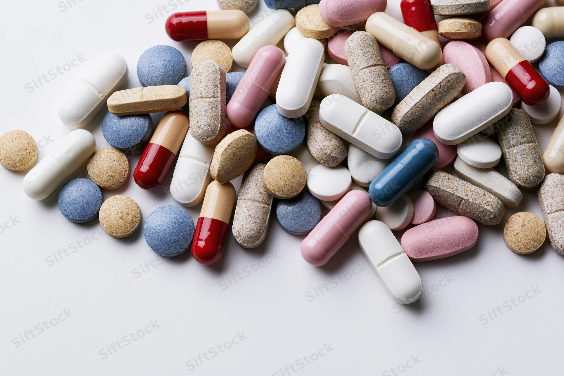 Assorted prescription pills and capsules scattered on a white surface