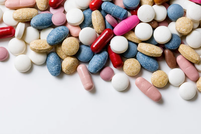 Assorted prescription pills and capsules scattered on white surface with copyspace below