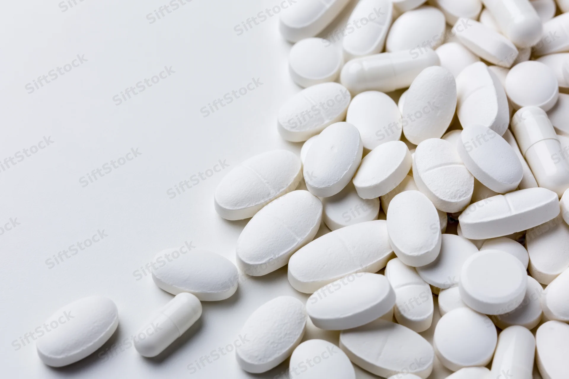 White pharmaceutical tablets and capsules scattered on a plain white surface
