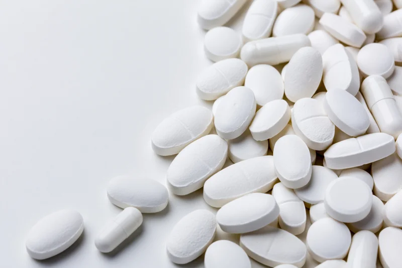 White pharmaceutical tablets and capsules scattered on a plain white surface