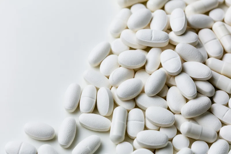 White pharmaceutical tablets and capsules scattered on a plain surface with copyspace