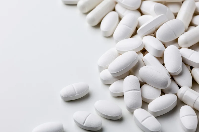 White pharmaceutical tablets and capsules scattered on a plain surface with copyspace