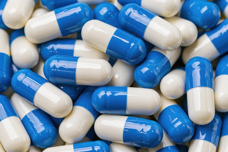 Blue and white gelatin capsules scattered in a heap, close-up view