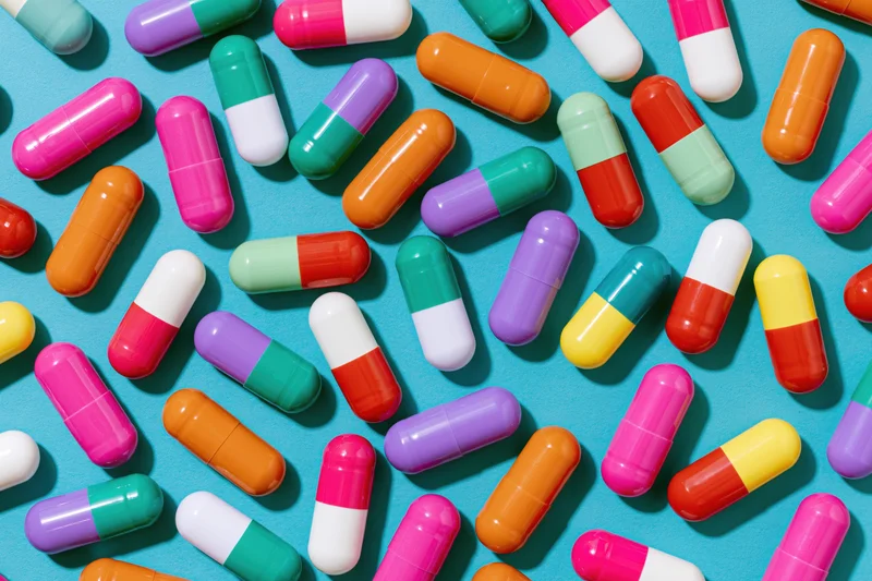 Colorful two-tone pharmaceutical capsules scattered on a blue background in a flat lay top view
