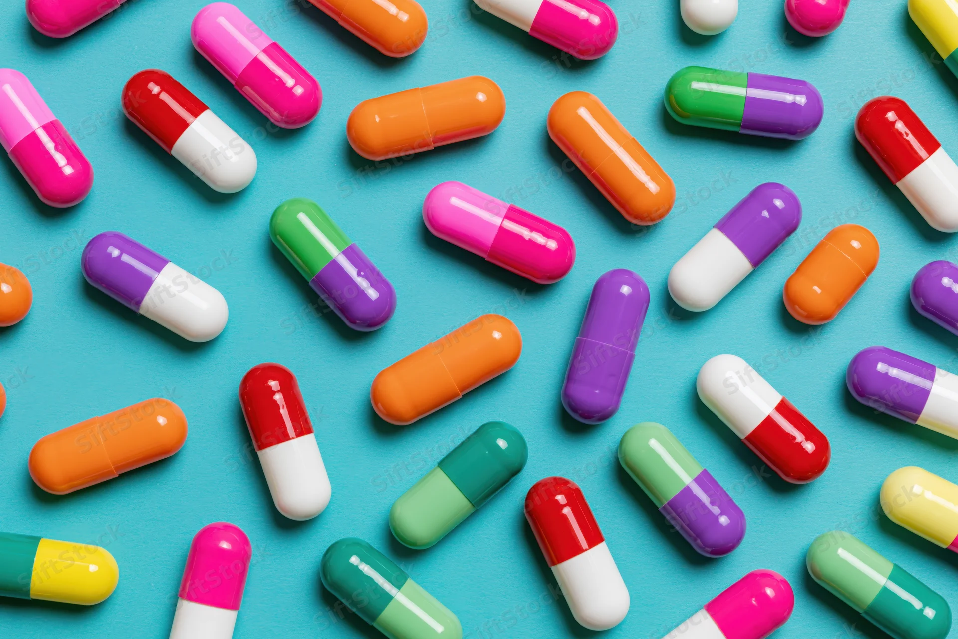 Colorful two-tone pharmaceutical capsules scattered on a blue background