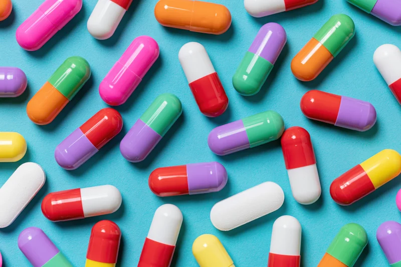 Colorful two-tone pharmaceutical capsules scattered on a blue surface in a flat lay view