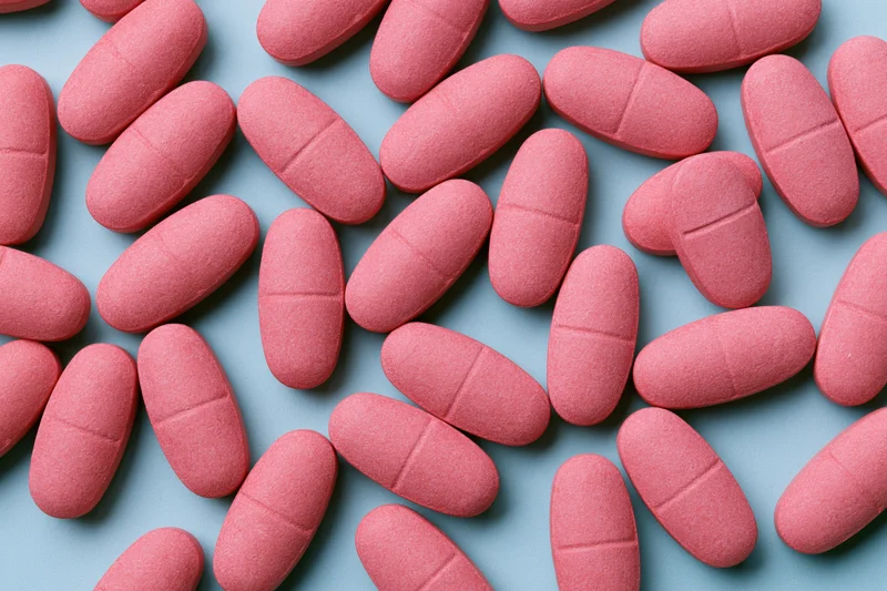 Matte pink oval caplet tablets scattered randomly on a blue surface
