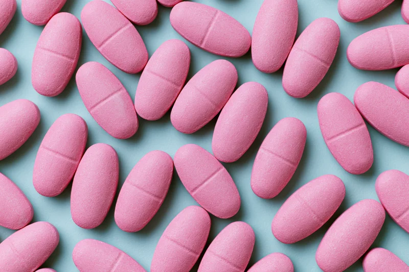 Scattered matte pink oval caplet tablets on a light blue surface