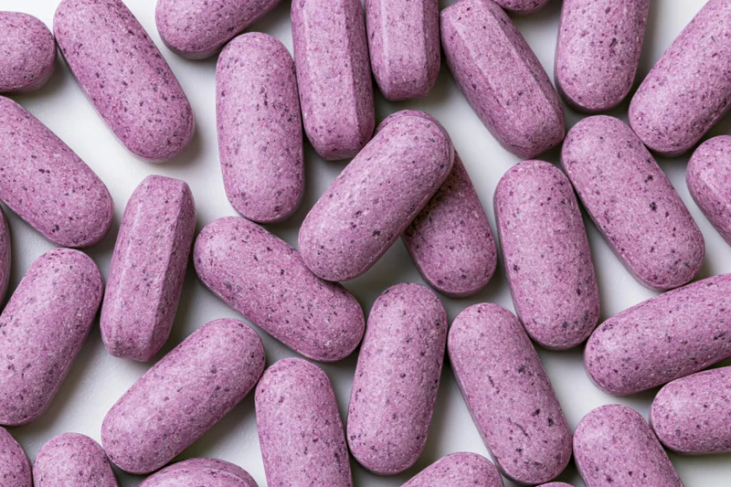Scattered oblong purple vitamin tablets on white surface