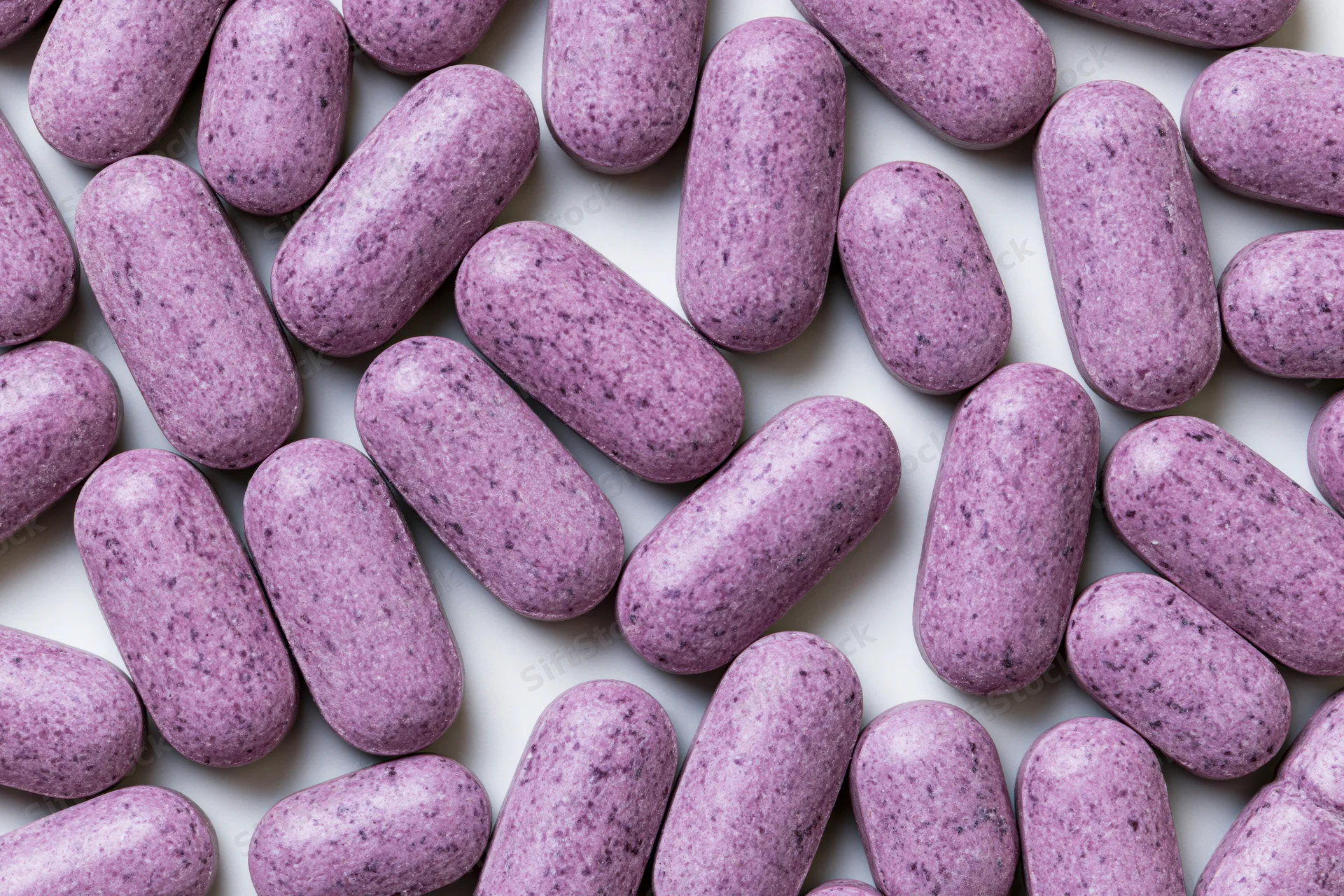 Oblong purple vitamin tablets scattered flat on white surface