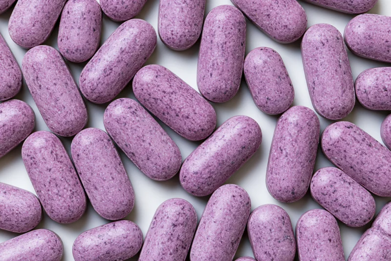Oblong purple vitamin tablets scattered flat on white surface