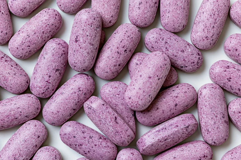 Oblong purple vitamin tablets scattered flat on white surface