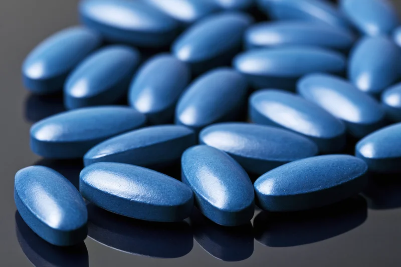 Blue coated oval tablets scattered on a reflective dark surface