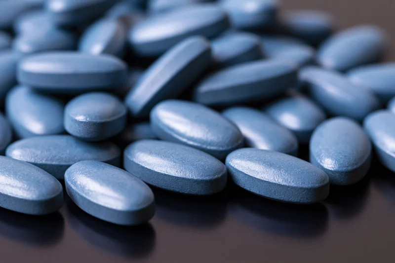 Blue coated oval tablets scattered on a dark surface in closeup view