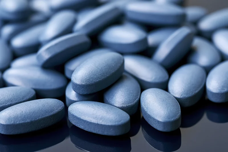 Blue coated oval tablets scattered on a reflective surface
