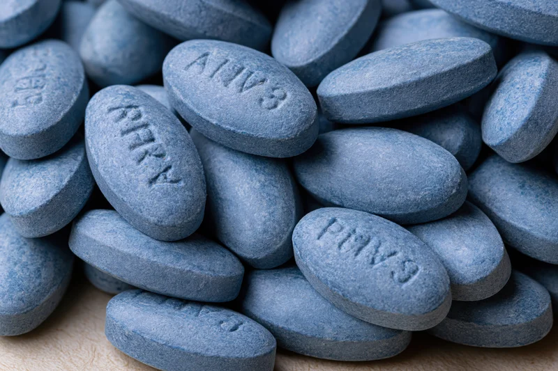 Pile of oval blue pharmaceutical tablets on wooden surface