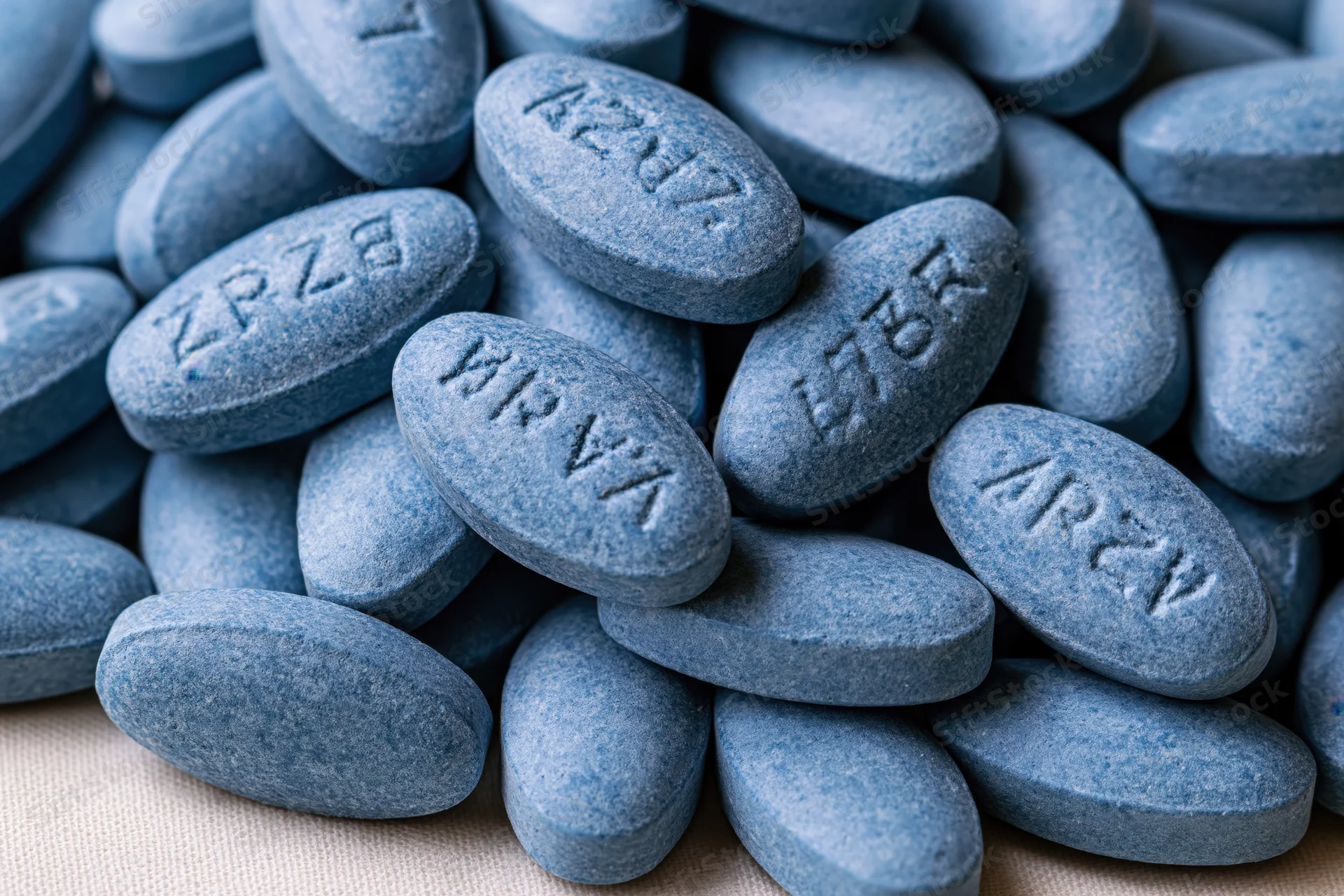 Blue oval pharmaceutical tablets piled loosely on a textured surface