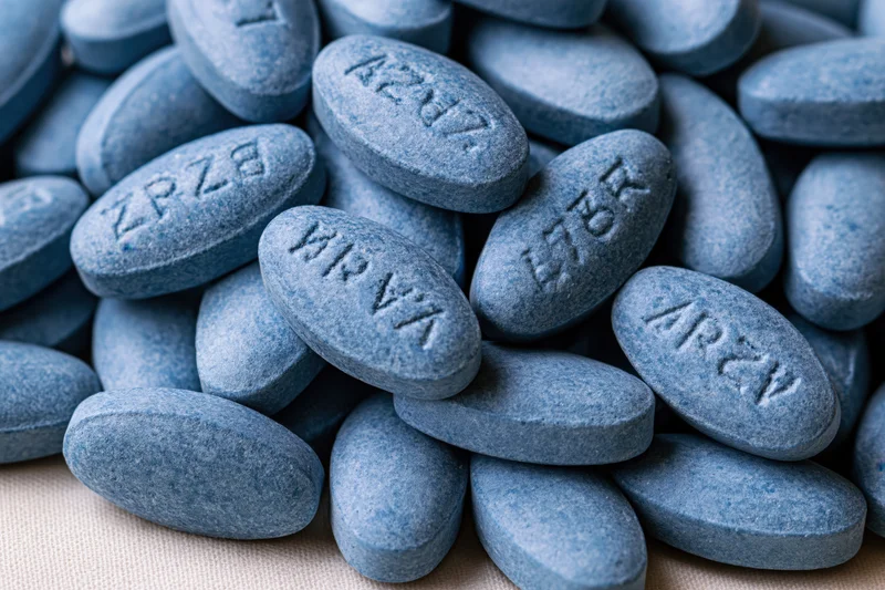 Blue oval pharmaceutical tablets piled loosely on a textured surface