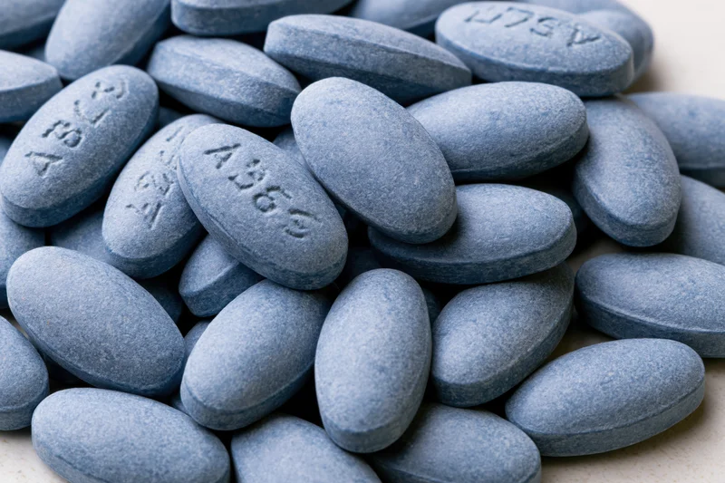 Pile of oval blue pharmaceutical tablets on a light surface