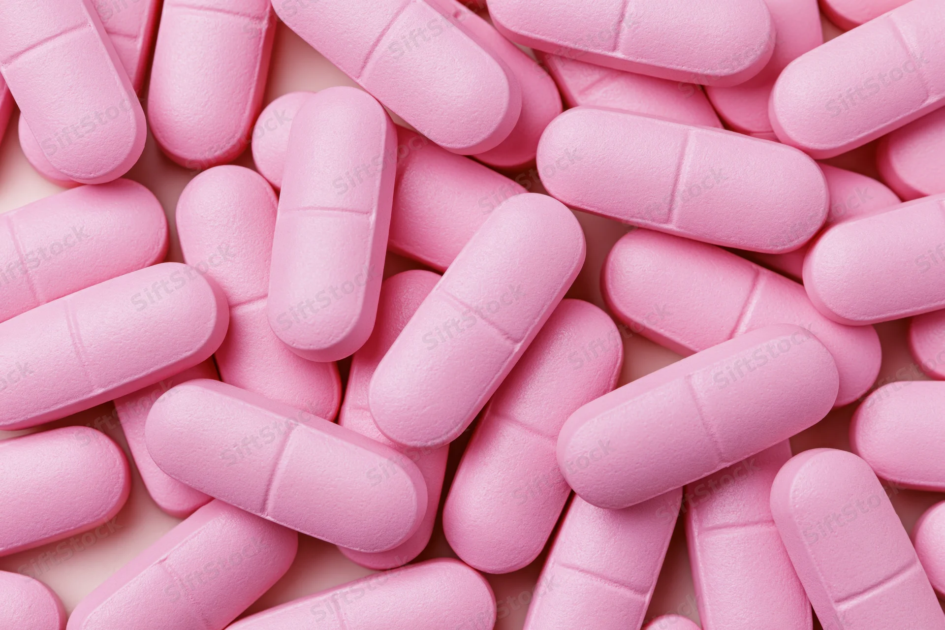 Pink supplement tablets scattered in a dense pile on a plain surface
