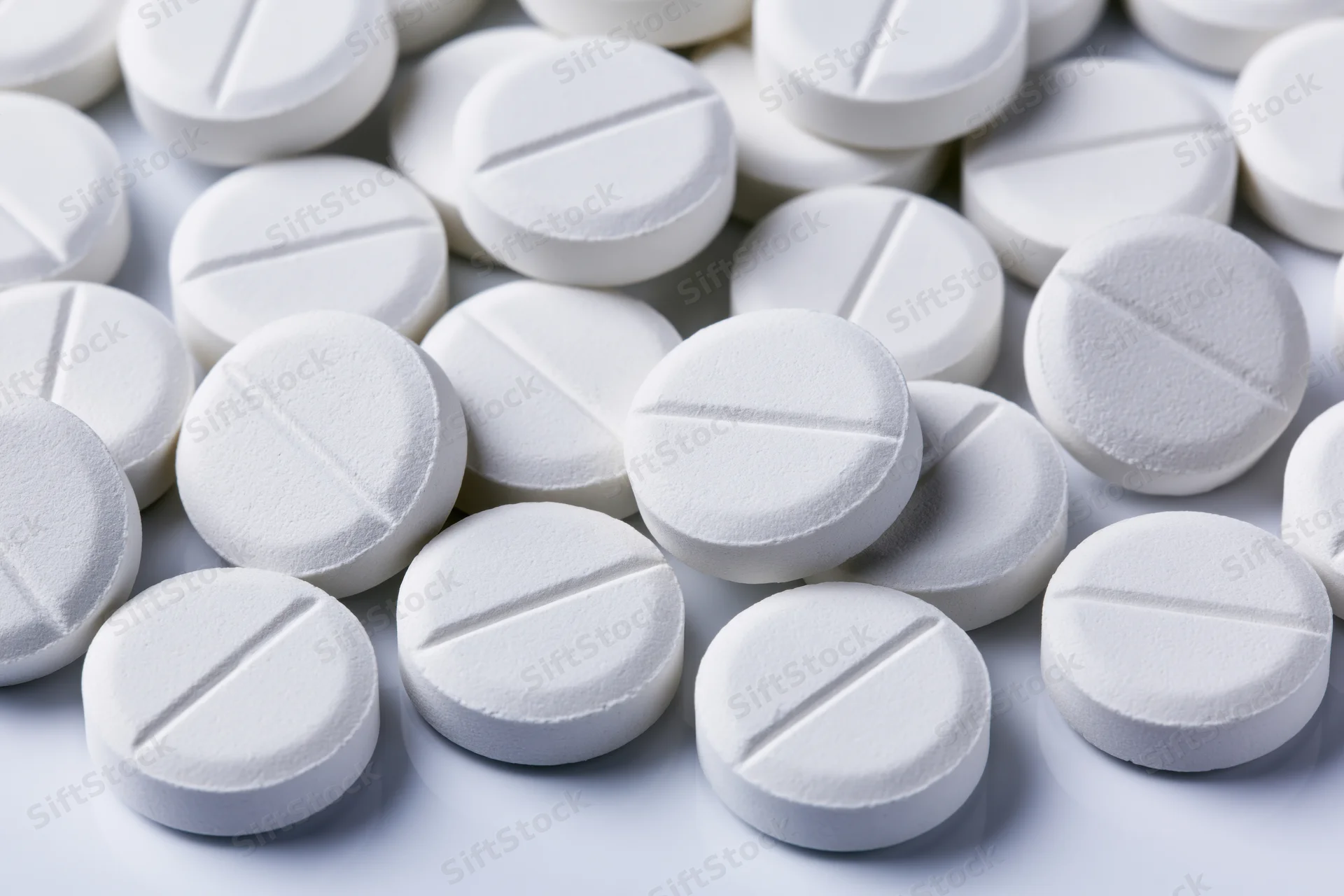 Close-up of round white pharmaceutical tablets with score lines on a white surface