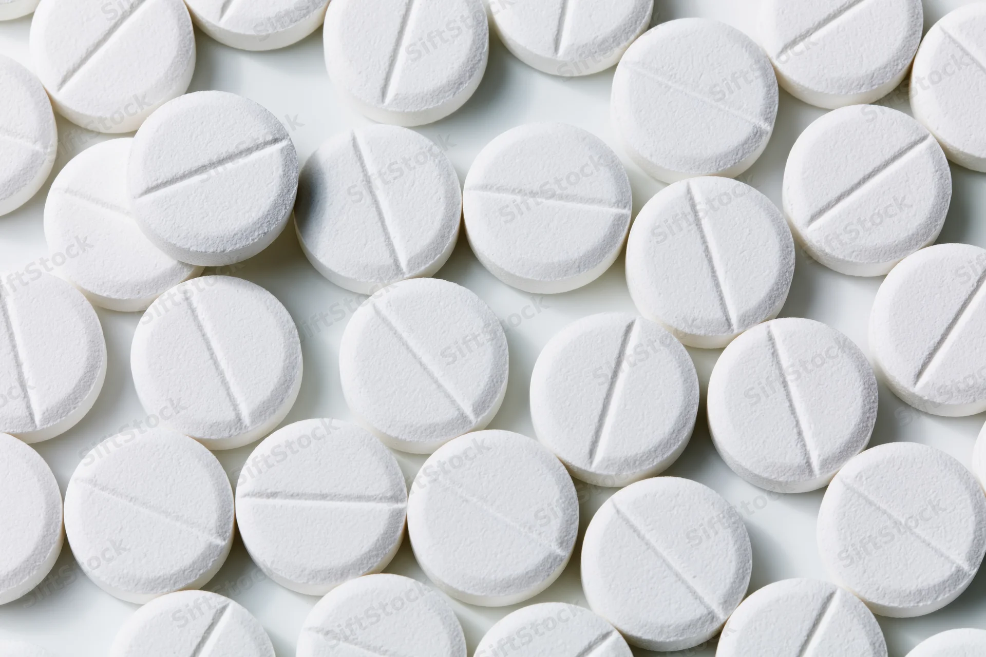Round white pharmaceutical tablets with score lines scattered on a plain white surface