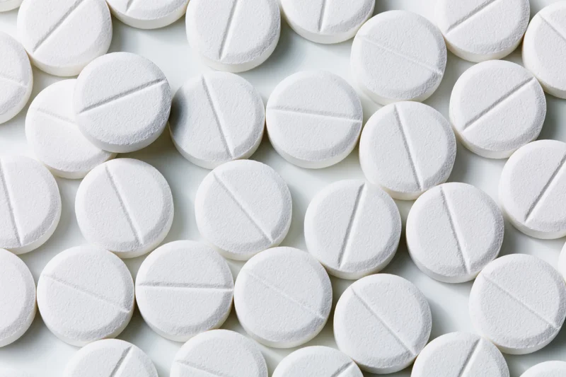 Round white pharmaceutical tablets with score lines scattered on a plain white surface