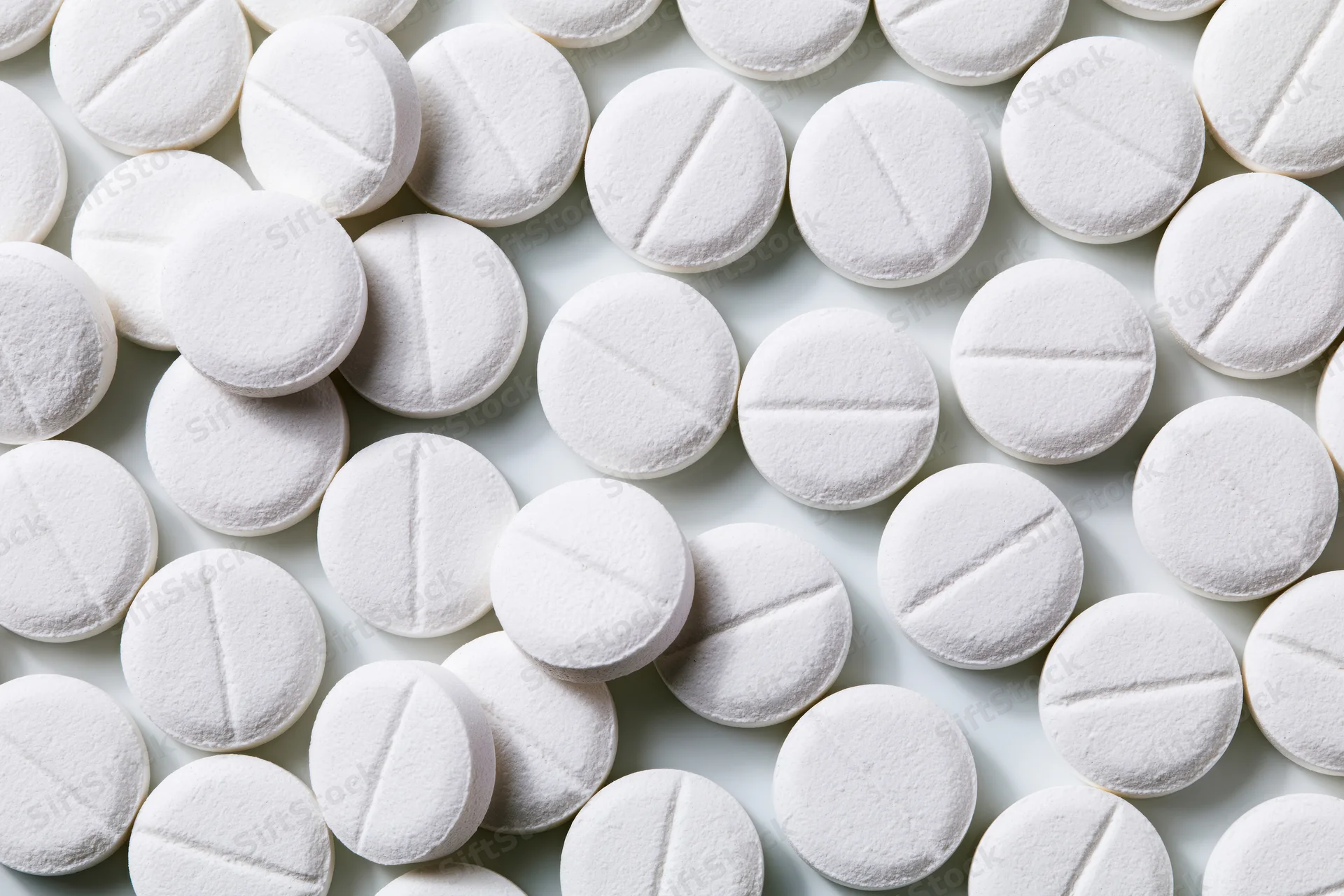 Round white pharmaceutical tablets with score lines scattered on a plain surface
