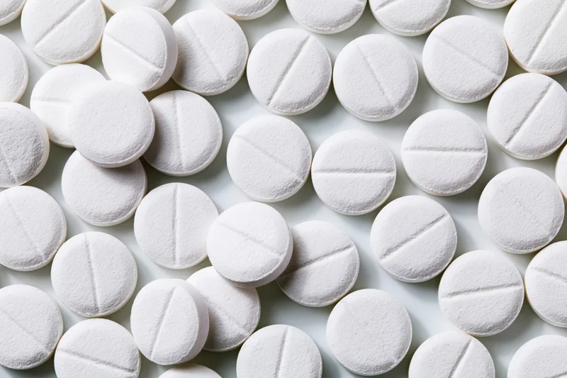 Round white pharmaceutical tablets with score lines scattered on a plain surface