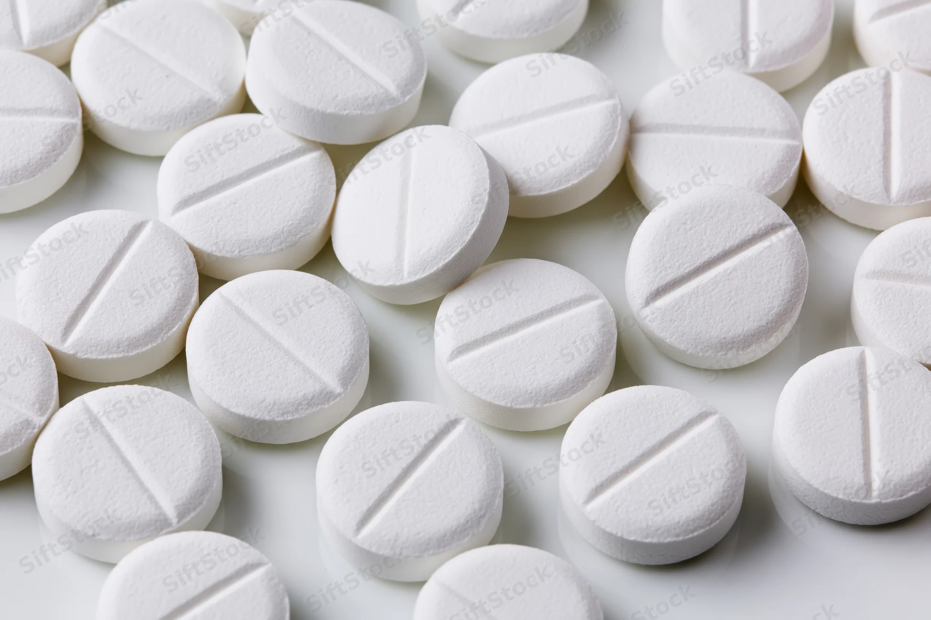 Round white pharmaceutical tablets with score lines scattered on a white surface