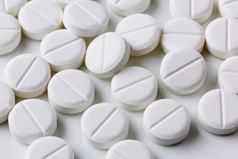 Round white pharmaceutical tablets with score lines scattered on a white surface