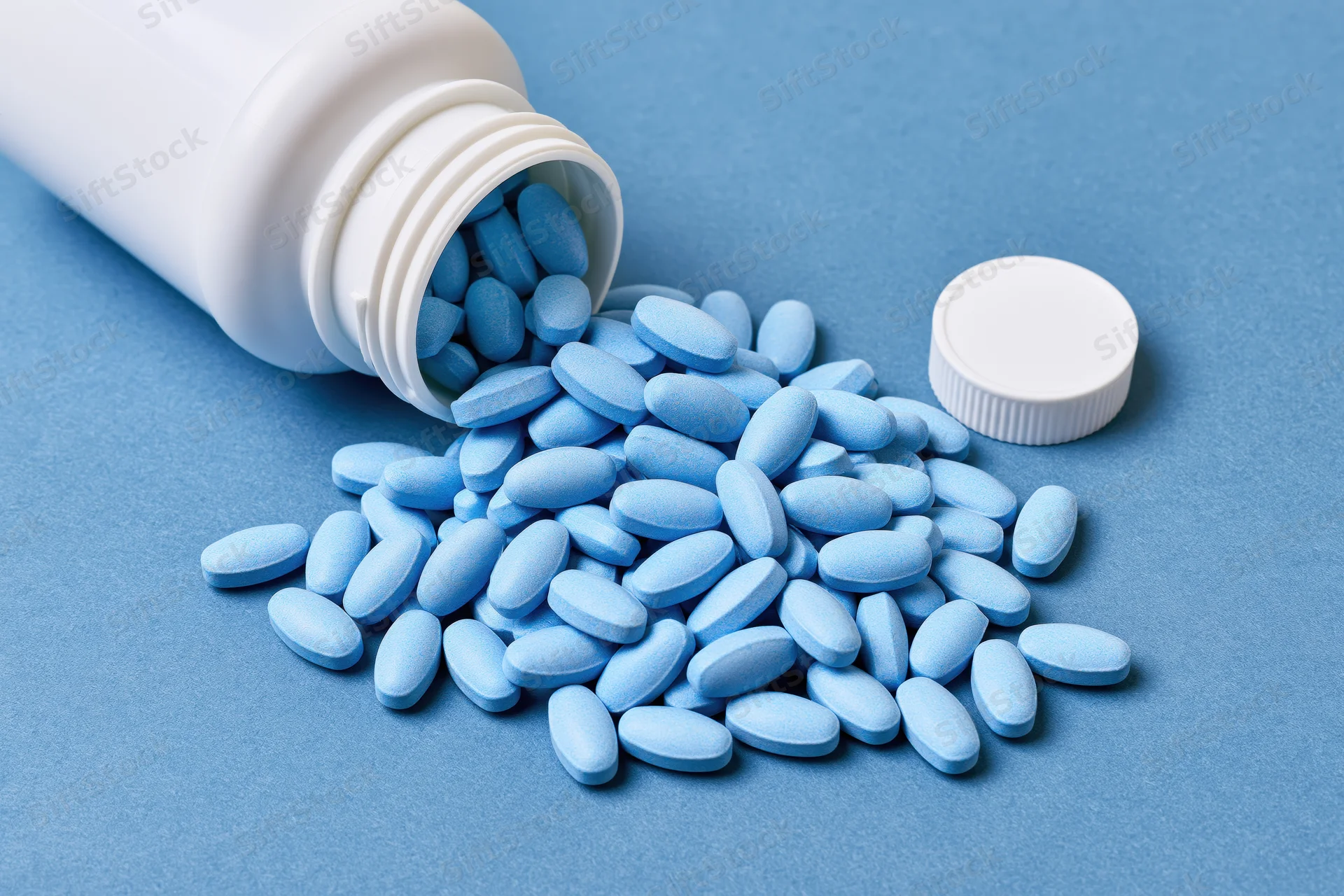 Light-blue oval pills spilling from a white bottle onto a blue surface