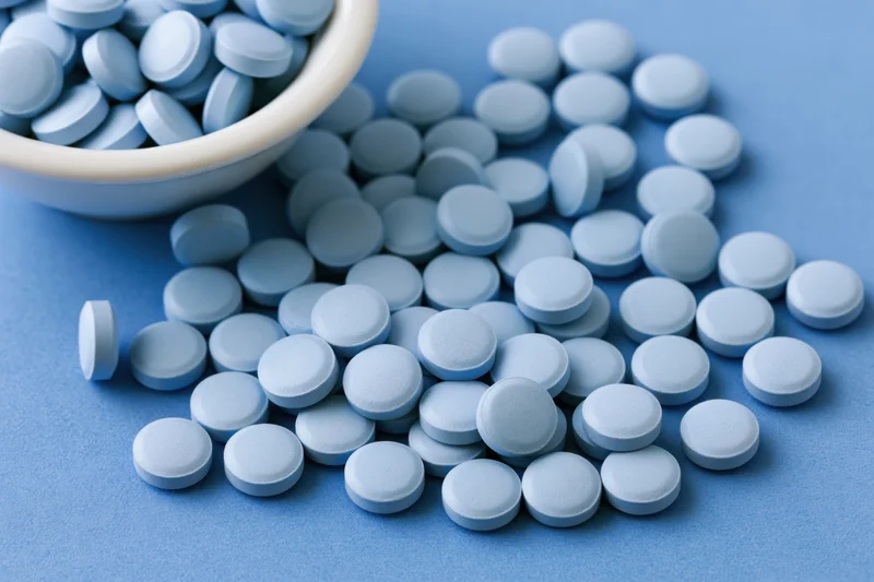 Light-blue pills scattered across a blue surface with a ceramic bowl holding more pills