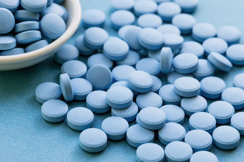 Light-blue pills scattered across a flat surface with a ceramic bowl in the corner