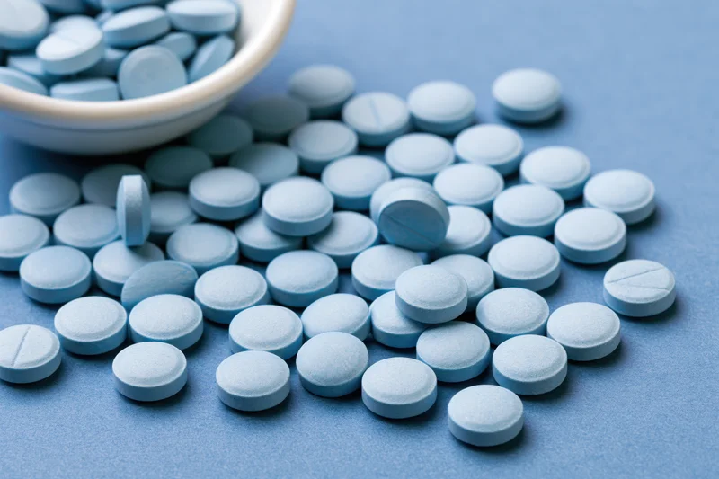 Light-blue pills scattered across a flat surface with a white bowl in the background