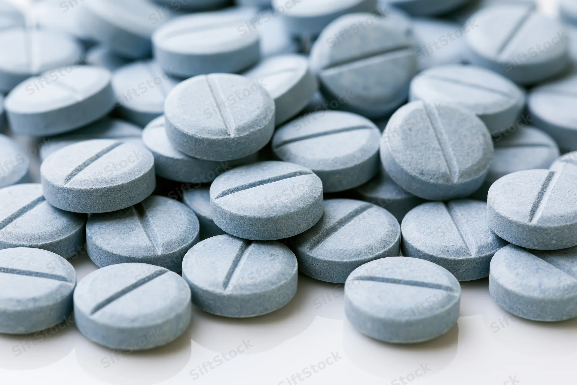 Pale blue pharmaceutical tablets scattered on a white surface in closeup view