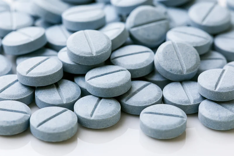 Pale blue pharmaceutical tablets scattered on a white surface in closeup view