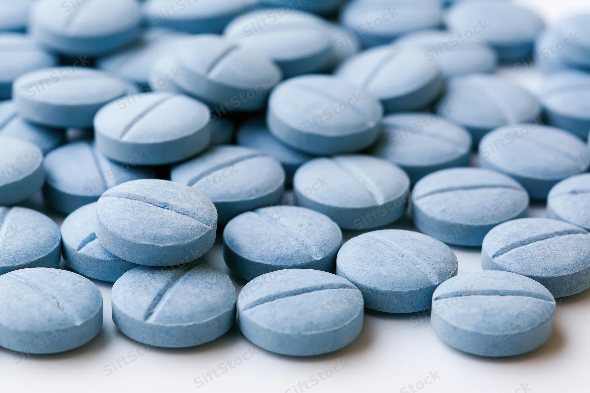 Pale blue pharmaceutical tablets scattered on a white surface