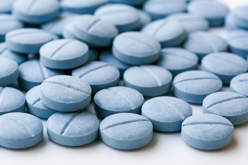 Pale blue pharmaceutical tablets scattered on a white surface