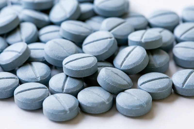 Pale blue pharmaceutical tablets scattered on a white surface