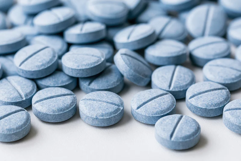 Scattered pale blue pharmaceutical tablets on a white surface in closeup view