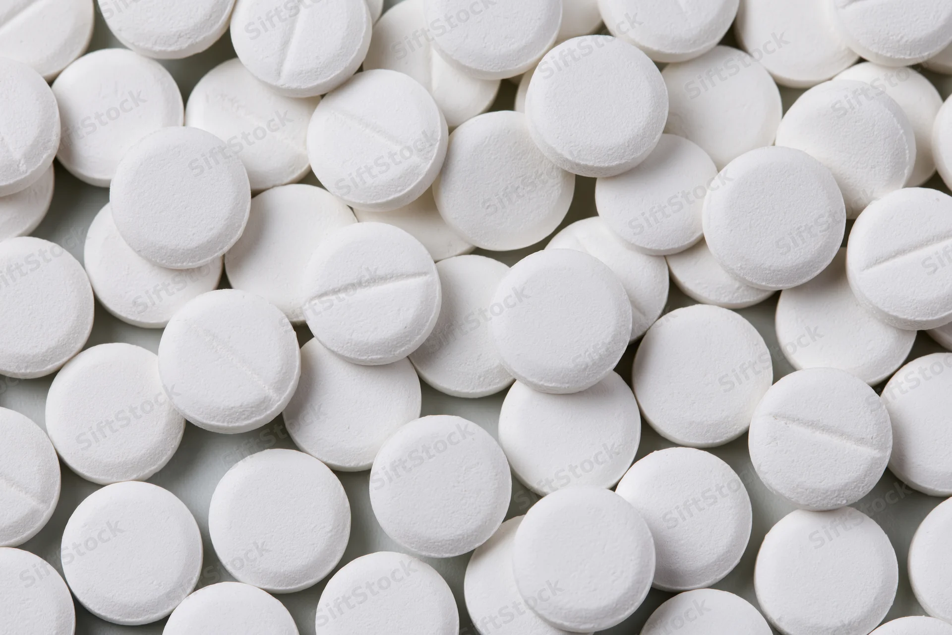 Scattered white round pharmaceutical tablets on a flat surface