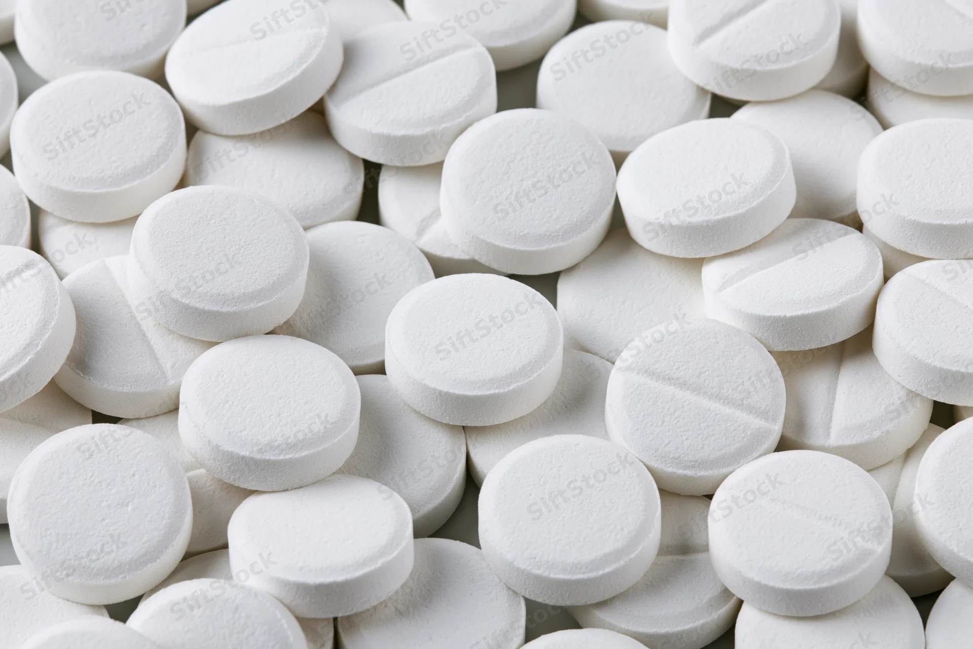 Scattered white round pharmaceutical tablets on a plain surface