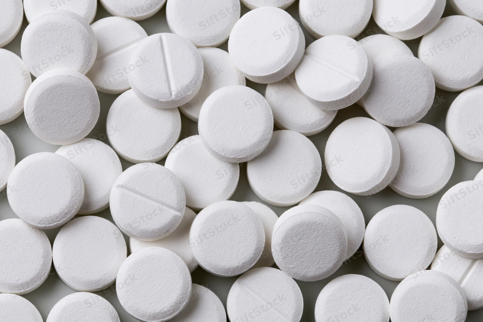Scattered white round pharmaceutical tablets on a flat surface