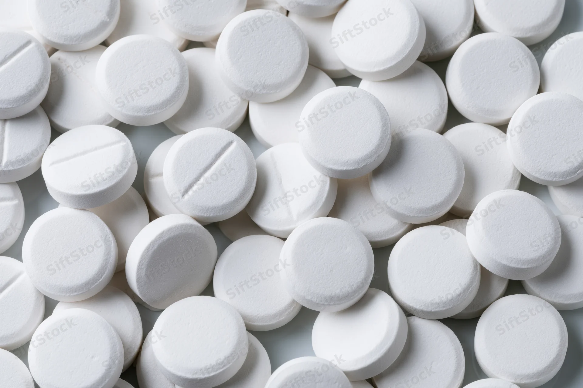 Scattered white round pharmaceutical tablets on a plain surface